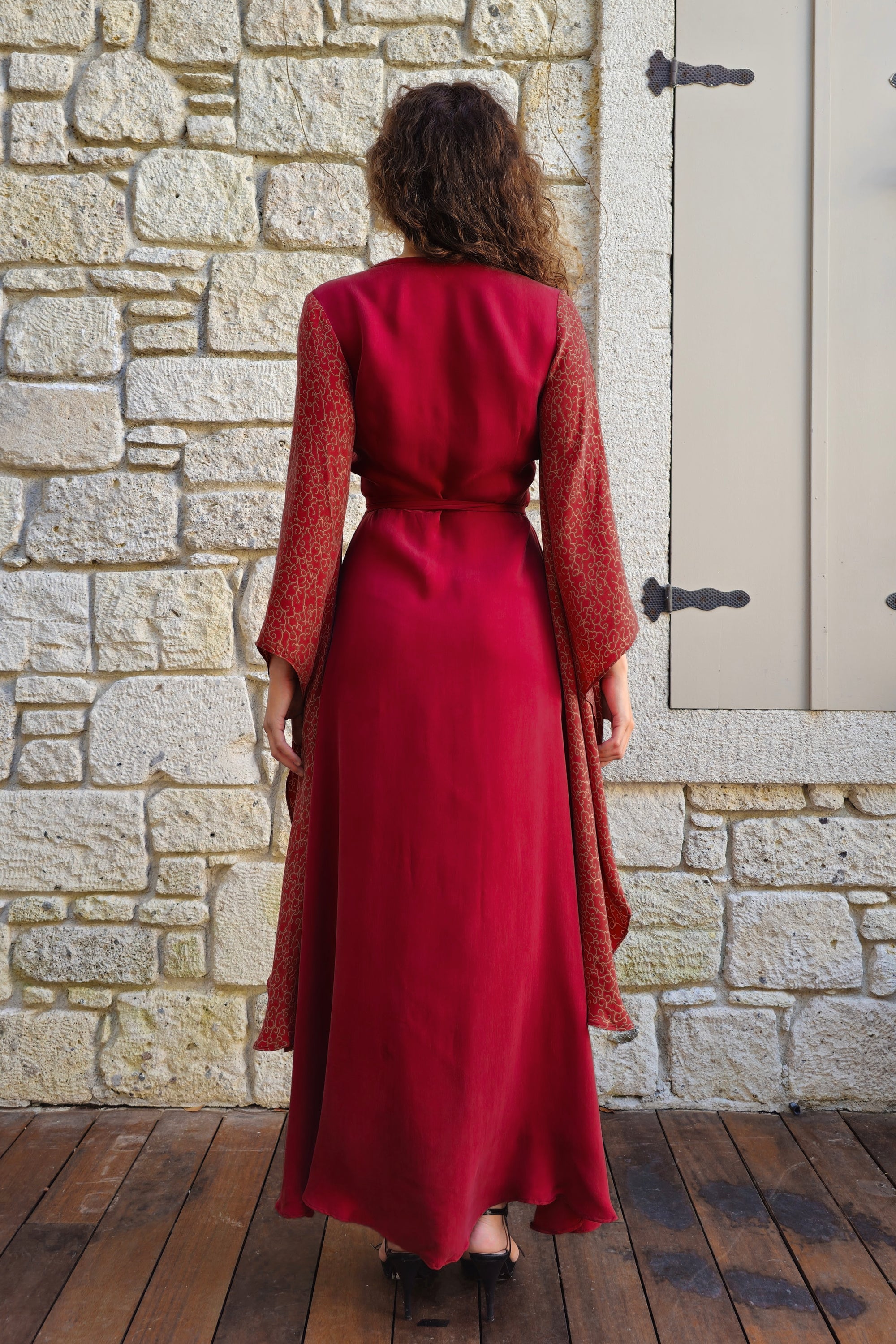 Person wearing a red dress standing in front of a stone wall.