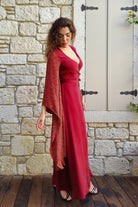 Woman in a red dress with a matching shawl standing against a stone wall.