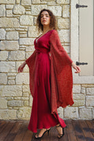 Woman in a red dress and matching cardigan standing against a stone wall.