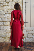 Person wearing a red dress standing in front of a stone wall.