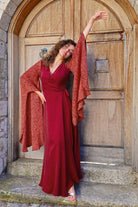Woman in a red dress with an orange shawl standing in front of a large wooden door.